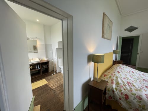 Chambre du Château de Vaux Morvan avec literie florale, mur d'accent jaune et salle de bains attenante