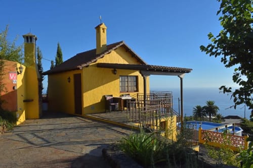 Villa amarilla con vistas al océano en Tijarafe, La Palma, con terraza, jardín y palmeras bajo cielo azul