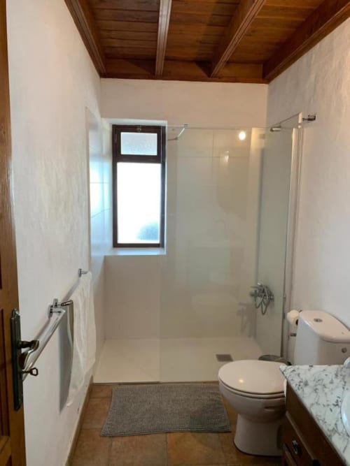Baño moderno en Villa El Topo con ducha amplia, inodoro, tocador de mármol, ventana, techo de madera y toallero calefactable