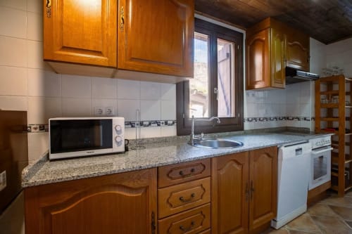 Cocina de madera con encimera de granito, electrodomésticos blancos y ventana con vistas a la montaña de Montgat en apartamento.