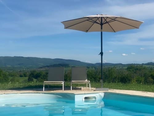 Piscine du resort avec parasol, chaises longues et paysage pittoresque du Morvan au Château de Vaux