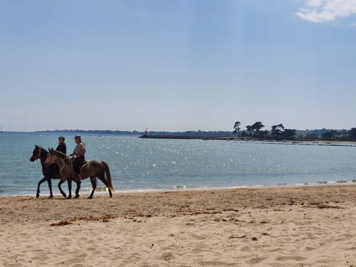 Two people horseback riding on sandy beach with turquoise water, La Fôret-Fouesnant coastal vacation rental