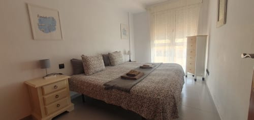 Helles Schlafzimmer in der Medano-Wohnung mit Doppelbett, Meerblick durch Terrassentüren, Holznachttisch und weißen Rollläden