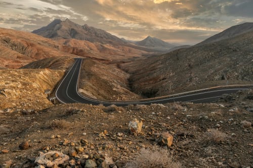 Route sinueuse à travers le désert volcanique près de Corralejo, Fuerteventura, pics dorés au coucher du soleil