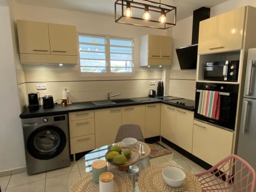 Cuisine et salle à manger modernes à l'appartement Kay Betty en Martinique avec armoires crème, comptoirs noirs et table à manger