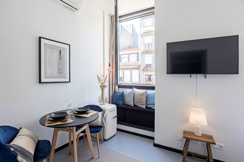 Estúdio compacto no Porto com mesa de refeições, assento azul, kitchenette, TV e vista para a cidade