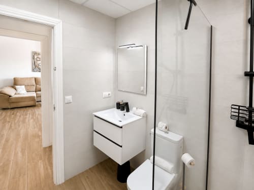 Modern bathroom in Apartamentos El Calón Playa with white vanity, mirror, toilet, and walk-in shower with black fixtures
