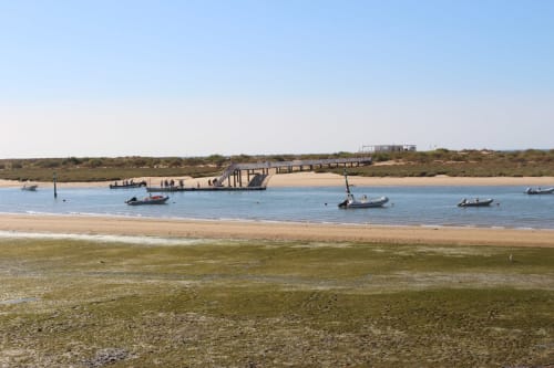 Tavira coastal beach with wooden pier, moored boats, and sandy shore at Break Lovers