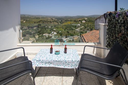 Vista panorámica desde la terraza de Casa lirio blanco con mesa azul decorada, asientos cómodos y vistas a los olivares de setenit de las bodegas