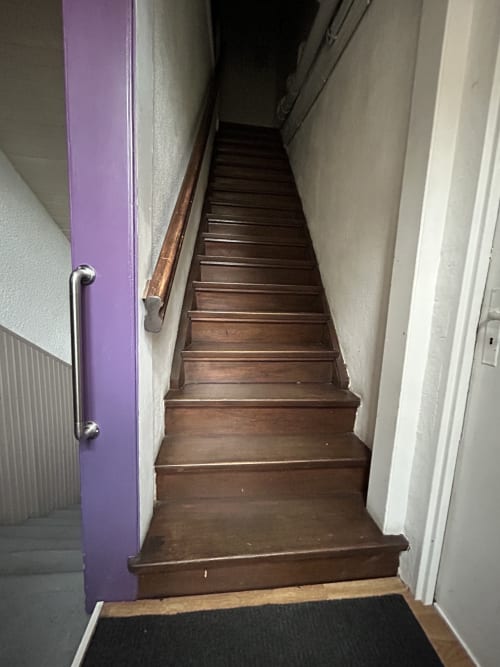 Escalier en bois aux marches brunes, encadrement de porte violet, rampe métallique et murs blancs à l'Hébergement Luxeuil Les Bains