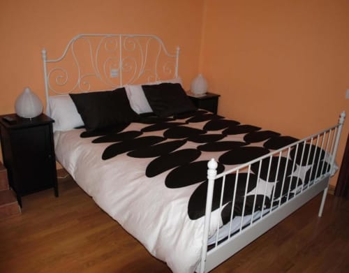 Dormitorio moderno con cama de estructura metálica blanca, ropa de cama en blanco y negro, paredes naranjas y mesillas oscuras en Casas Rurales La