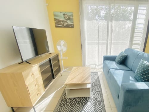 Séjour moderne de Maisons En Or à Sinnamary avec canapé bleu, meuble TV en bois, mur jaune et balcon