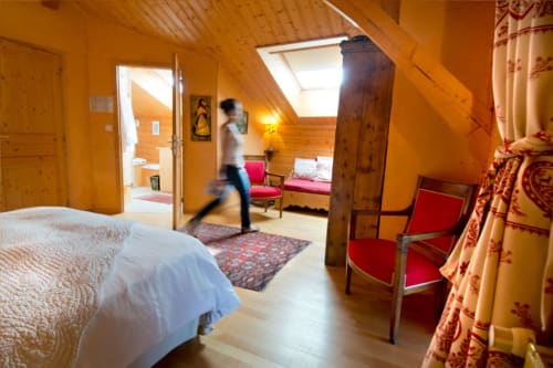 Chambre Art Pop spacieuse à l'Auberge Nemoz avec poutres en bois, lit, fauteuil rouge et velux donnant sur Le Haut-Bréda