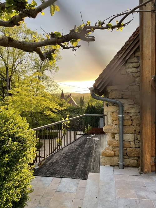 Terrasse en pierre aux Pratges, Figeac avec terrasse bois, balustrade métal, feuillage printanier et vue vallée