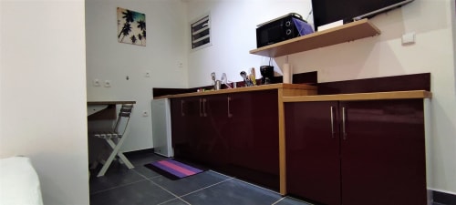 Kitchenette moderne du gîte Kaz A Bibi avec mobilier sombre, comptoirs en bois, TV écran plat et tapis de yoga à Sainte-Rose,