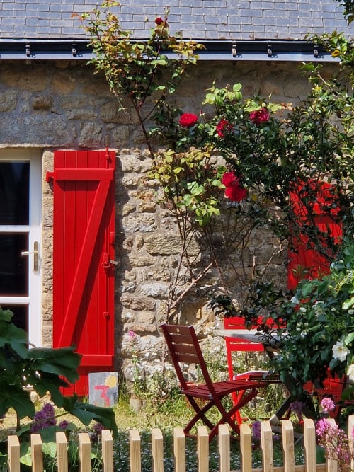 Vue charmante du jardin aux Chambres du Keriolet avec porte rouge, roses grimpantes et salon extérieur à La Trinité-sur-Mer