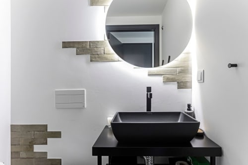 Banheiro moderno em hotel no Porto com pia preta, espelho redondo iluminado e acabamentos decorativos em pedra sobre branco