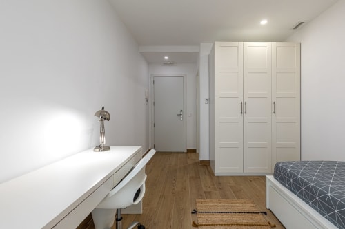 Modern bedroom at Residencia Demar in Godella with white wardrobe, desk, wooden flooring, and patterned bedding