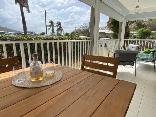 Table de salle à manger en bois sur la véranda couverte de l'appartement Kay Betty en Martinique avec vue sur le jardin et palmiers