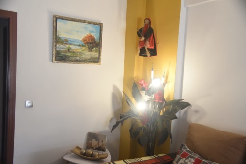 Benavente apartment interior with religious icon, landscape painting, flowers, and decorative items on table
