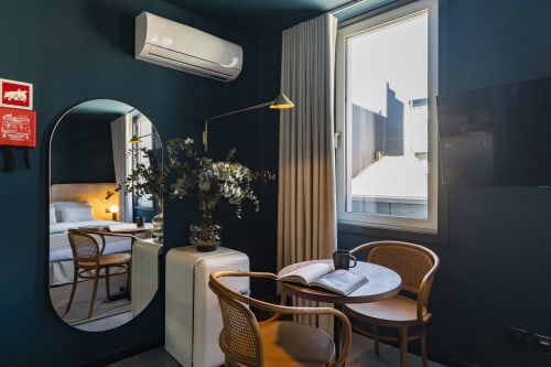 Estúdio de hotel moderno no Porto com paredes verde-azulado, cadeiras de madeira, mesa redonda e vista para a cidade pela porta da varanda