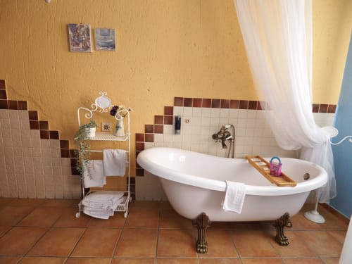 Baño elegante en apartamento rural español con bañera de patas, azulejos beige y cortinas con vista al jardín