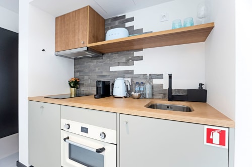 Kitchenette moderna no Benefit Collection Porto com prateleiras de madeira, armários brancos e painel traseiro em azulejo cinza