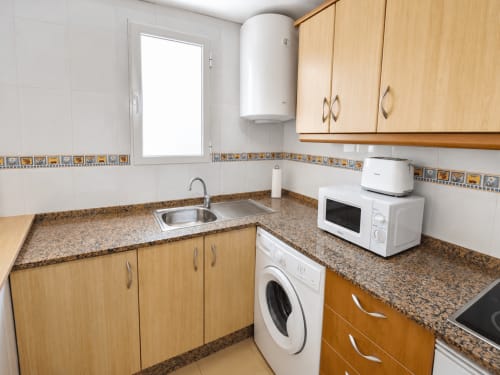 Cocina moderna en Apartamentos El Calón Playa con muebles de madera clara, encimeras de granito y electrodomésticos blancos