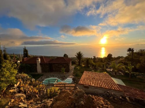 Vista al atardecer desde Villa Awara en La Palma con tejados escalonados, palmeras y paisaje mediterráneo al anochecer