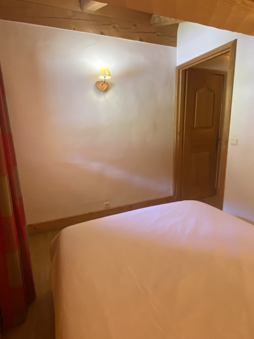 Chambre spacieuse à La Ferme des Georgières avec lit blanc, porte en bois et applique murale en forme de cœur