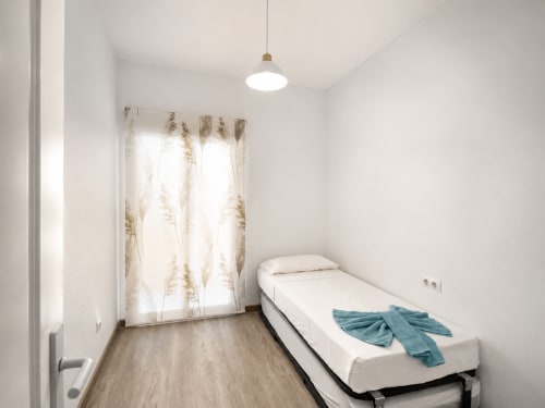 Dormitorio moderno en Apartamentos El Calón Playa con cama individual, lámpara colgante y puertas de patio con cortinas naturales