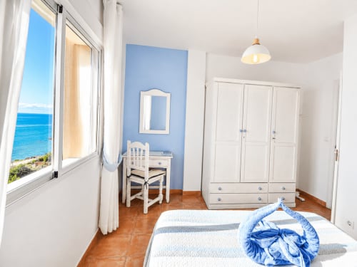 Bright seafront bedroom with blue accent wall, white wardrobe, sea views, terracotta floors at Apartamentos El Calón Playa,
