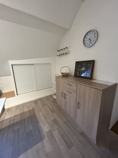 Studio moderne à Hébergement Luxeuil Les Bains avec commode en bois, horloge murale et décoration minimaliste à Luxeuil-les-Bains