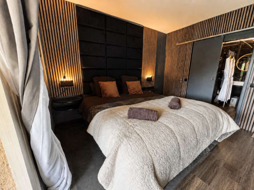 Suite de luxe à Domaine Valenquercy avec mur à boiseries, lit moderne, éclairage ambiant et équipements spa