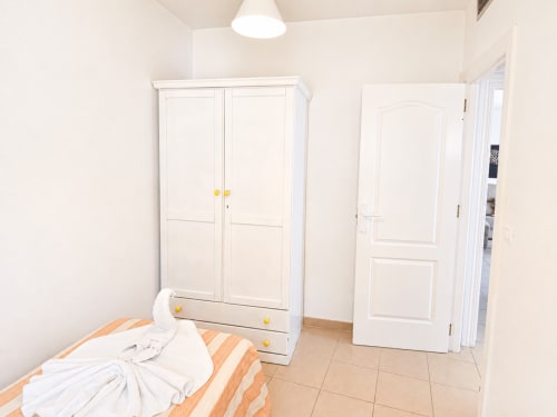 Luminosa habitación en Apartamentos El Calón Playa con armario blanco, cama de rayas naranjas y piso de azulejos