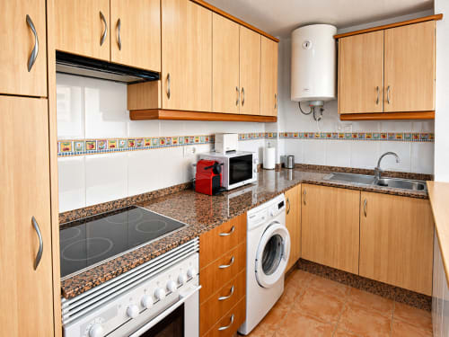 Modern kitchen in Apartamentos El Calón Playa with wood cabinets, granite countertops, white appliances and washing machine