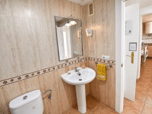Bathroom in Apartamentos El Calón Playa with pedestal sink, mirror, toilet, and beige tile walls