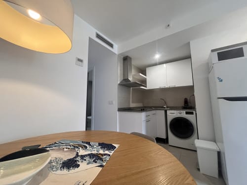 Modern kitchen in Corralejo apartment with white cabinets, washing machine, and wooden dining table