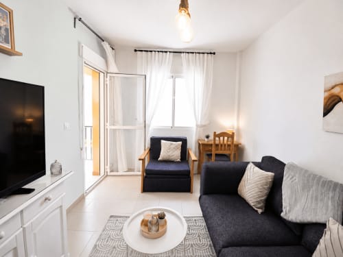 Moderno salón con sofá negro, sillón, televisor y balcón amueblado en Apartamentos El Calón Playa, Cuevas del
