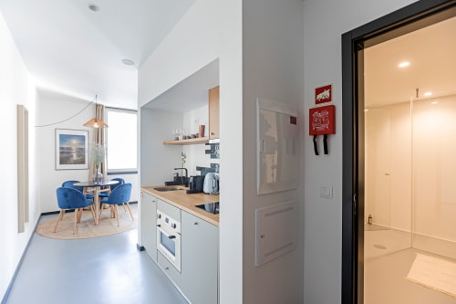 Moderno e superior apartamento estúdio no Porto com kitchenette, área de refeições, cadeiras azuis e entrada do banheiro