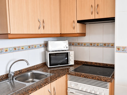 Modern kitchen with wooden cabinets, granite countertop, white appliances, and decorative blue tile backsplash at