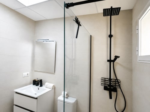 Modern bathroom with walk-in shower, black rainfall showerhead, white sink vanity, and mirror at Apartamentos El Calón Playa.