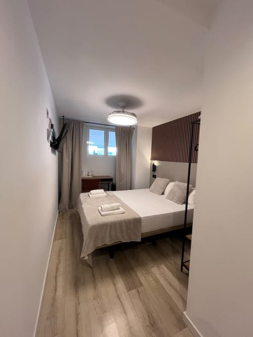 Habitación estándar moderna en Hostal Abacoa de Alicante con cama doble, suelo de madera y vistas a la ciudad desde la ventana