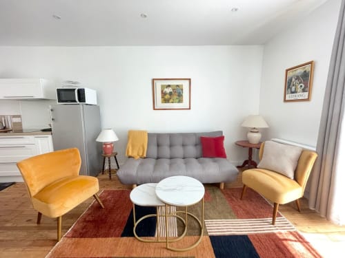 Séjour moderne de l'appartement Le 58 Bayeux avec canapé gris, chaises jaunes et kitchenette équipée
