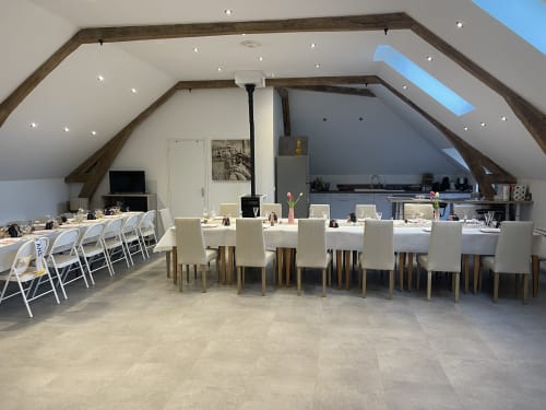 Spacious attic dining area at Les Gites De Flaubert cottage with long table, kitchen, and skylight