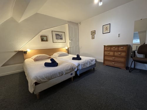 Chambre spacieuse à Hébergement Luxeuil Les Bains avec deux lits jumeaux, commode en bois et vue sur la ville dans une mansarde lumineuse