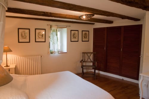 Spacieuse chambre à Maison d'Andressac avec poutres en bois, lit blanc et vue sur le jardin.
