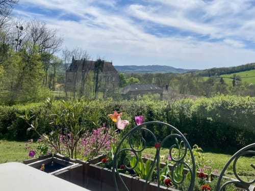 Vue du jardin du Château de Vaux Morvan avec tulipes, haie et château médiéval dominant la campagne d'Étang-sur-Arroux