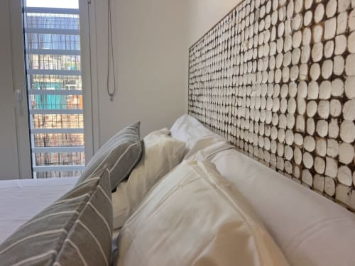 Modern bedroom with white bedding and geometric patterned headboard, bookshelf visible through window in Corralejo apartment