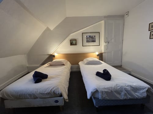 Deux lits jumeaux dans un studio mansardé moderne à Hébergement Luxeuil Les Bains avec tête de lit en bois et éclairage ambiant